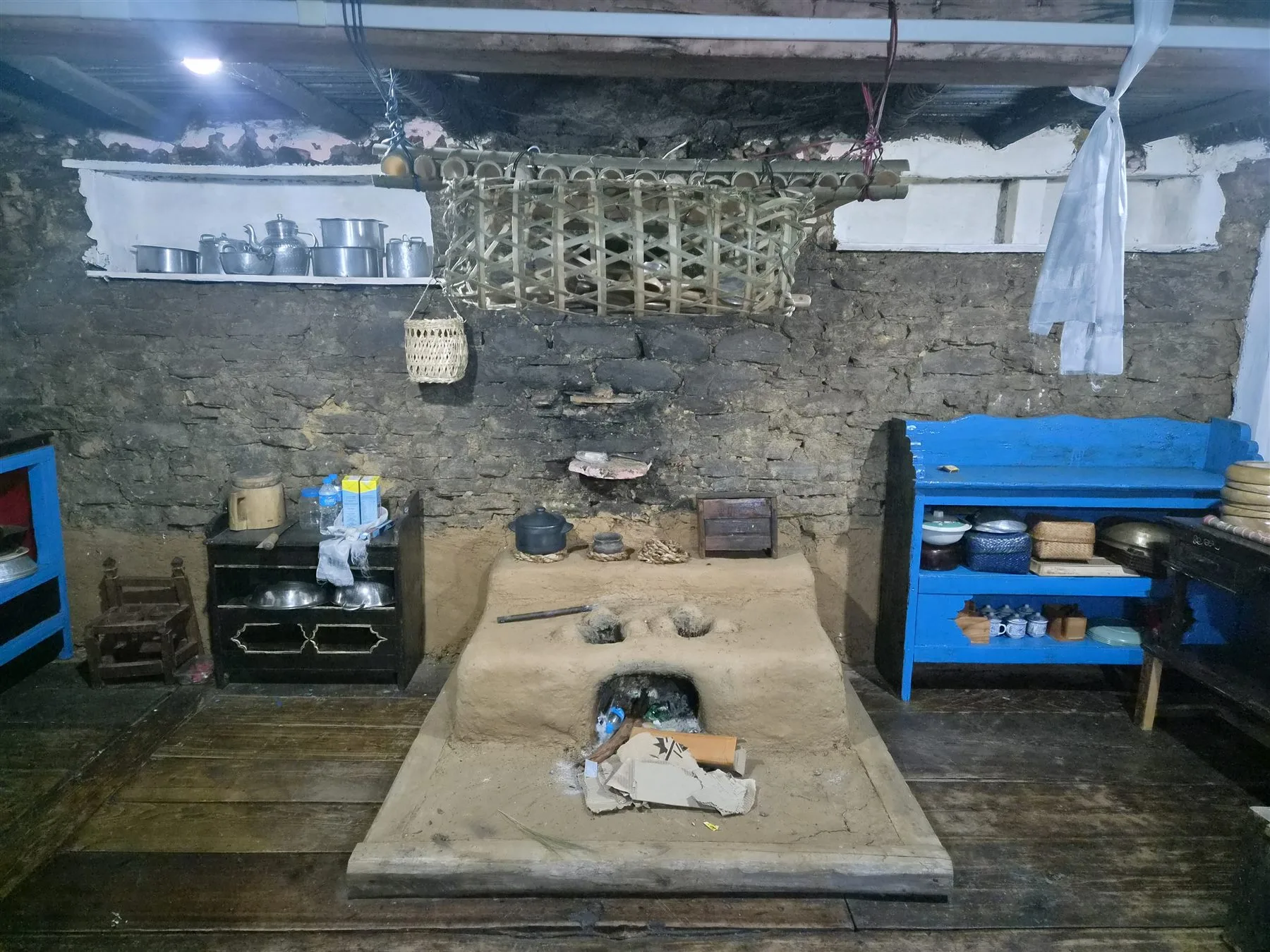 Traditional clay hearth with black pots beneath bamboo storage